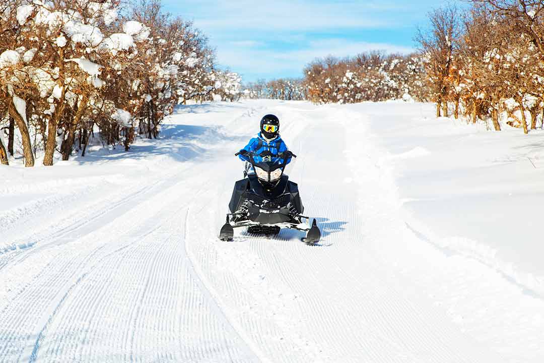 A person riding a snowy road in a black snowmobile